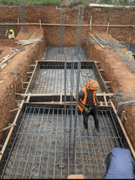 Slide 1 &mdash; Construction site showing workers setting up steel reinforcement bars in a foundation pit, surrounded by earth and wooden supports.