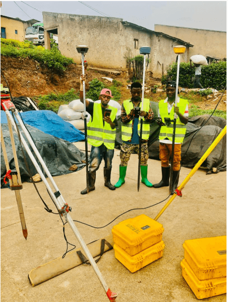 Slide 4 &mdash; Three workers in reflective vests and boots stand on a construction site, holding surveying equipment amidst a backdrop of equipment and greenery.